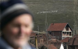Un home na vila albano-cosovar de Kmetovce, coa palabra 'Serbia' en serbio ao fondo